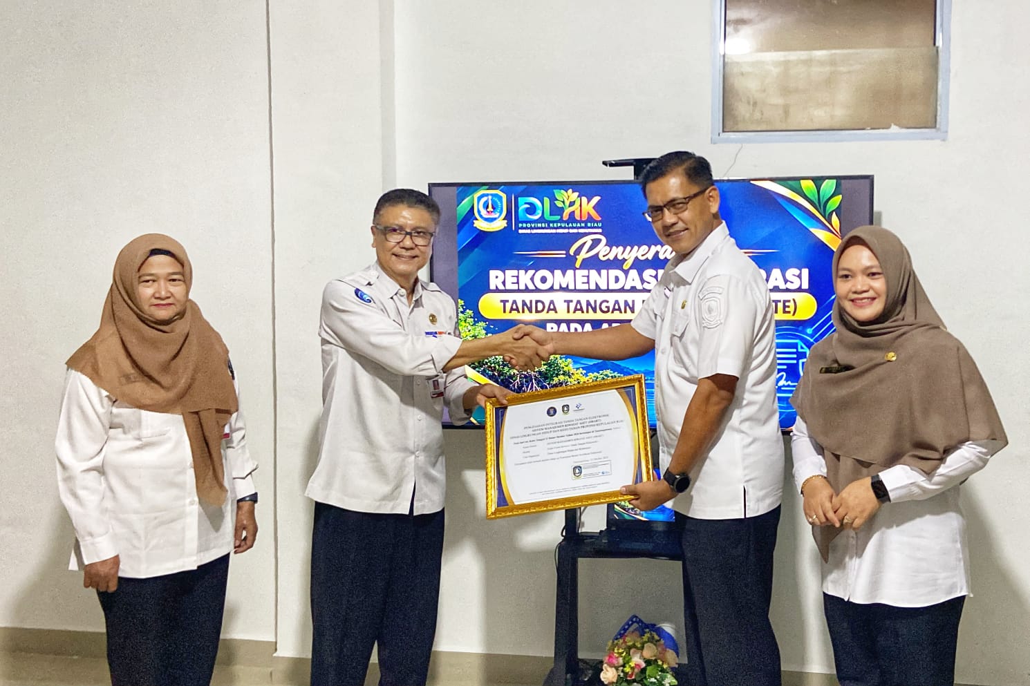Sekretaris Diskominfo Kepri, James Simon Pattikawa didampingi Kepala Bidang Statistik dan Persandian Diskominfo Kepri Dwi Anggraini, menyerahkan Piagam Pengesahan Integrasi TTE Aplikasi SMART kepada Kepala DLHK Kepri Indra Hidayat, Kamis (22/10/2026). 